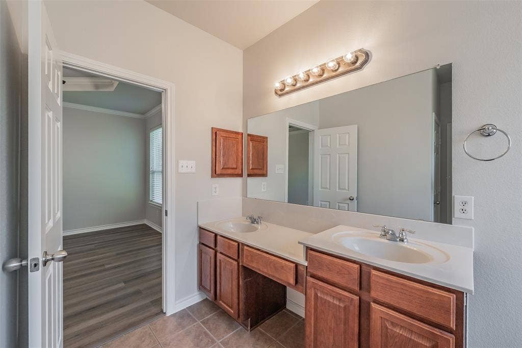 2205 Clairborne Drive, Fort Worth, TX 76177 Double vanity with integrated sinks, expansive wall-mounted mirror, and warm wood-finish cabinetry