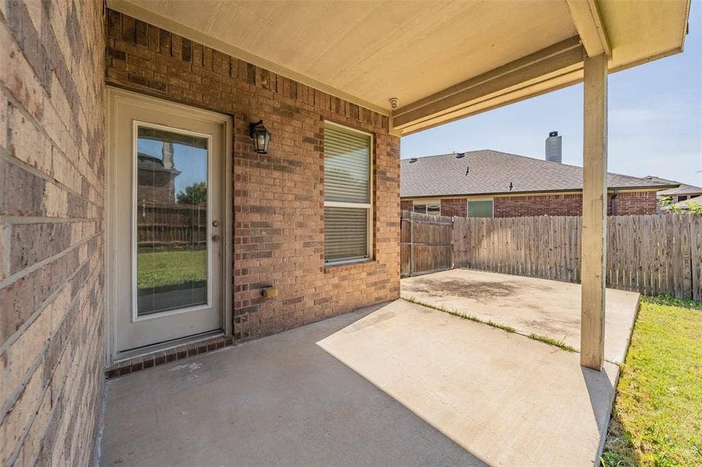 2205 Clairborne Drive, Fort Worth, TX 76177 Covered concrete patio with brick exterior, featuring an exterior door with integrated window blinds and an exterior light fixture
