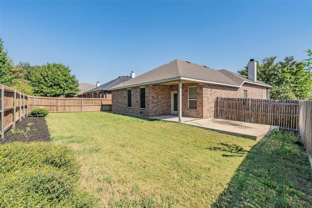 2205 Clairborne Drive, Fort Worth, TX 76177 Fenced backyard featuring a covered patio, additional concrete pad, brick exterior, and a shingle roof