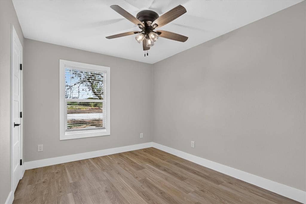 Wood-finish flooring, neutral gray walls, white trim, and a ceiling fan with integrated lighting