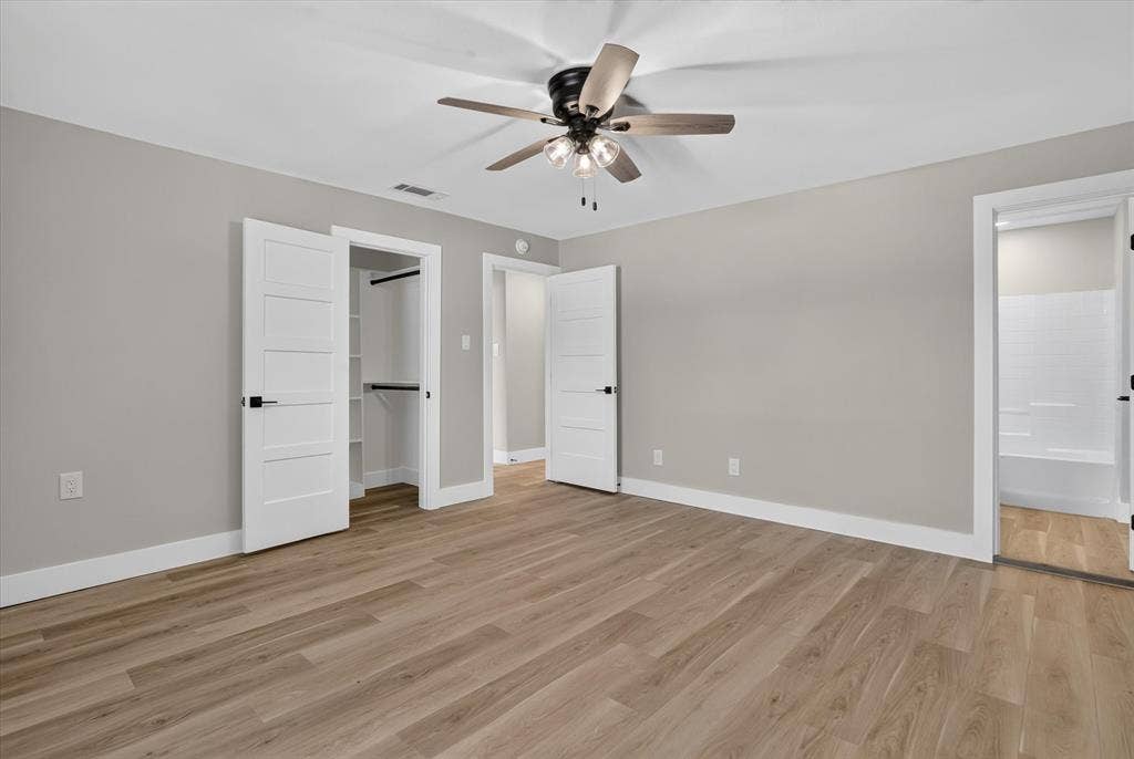 Wood-finish flooring with light gray walls, a ceiling fan with integrated lighting, a built-in closet with shelving, and a white paneled door