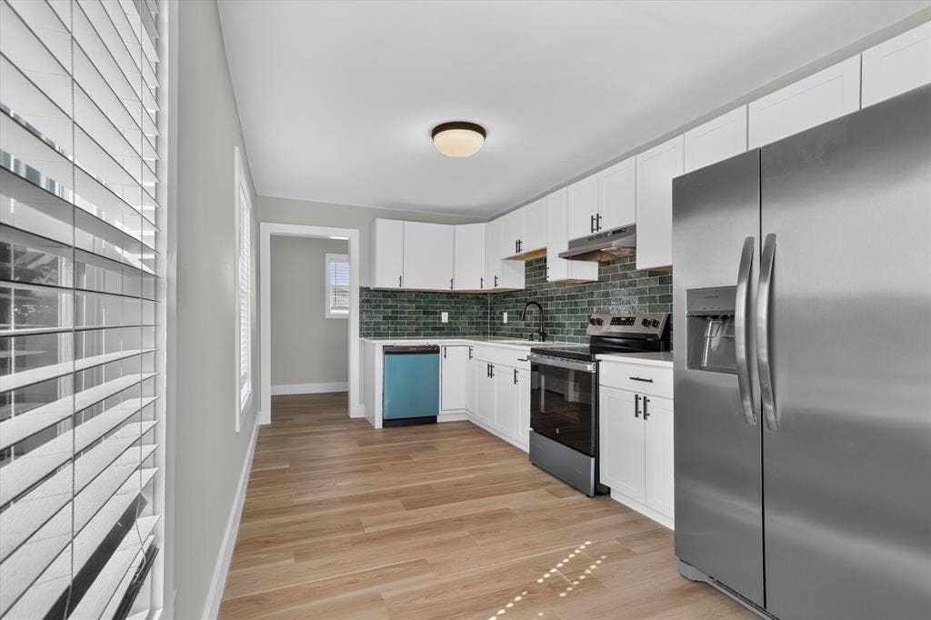 Contemporary kitchen featuring white cabinetry, stainless steel appliances, a unique green tile backsplash, and wood-finish flooring