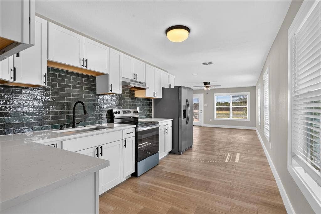 Contemporary kitchen featuring white cabinetry with brushed nickel hardware, stainless steel appliances including a gas range and refrigerator, dark subway tile backsplash, quartz countertops, and a waterfall-edge island