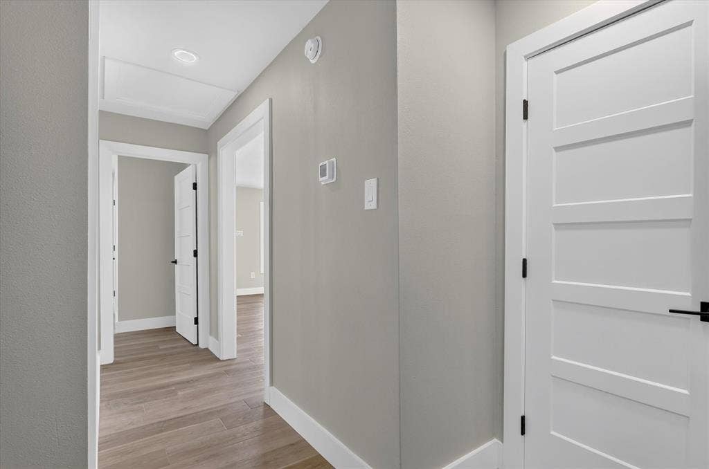 Hallway featuring wood-finish flooring, white trim, recessed ceiling lighting, and solid white doors with matte black hardware