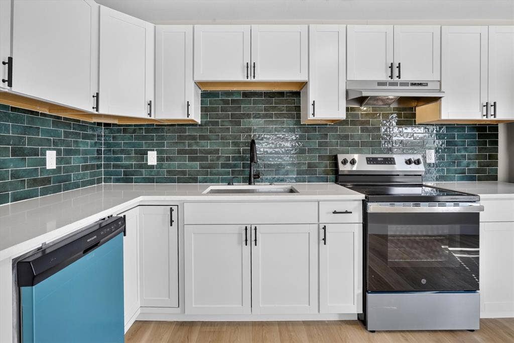 White shaker-style cabinetry with matte black hardware, a dark teal subway tile backsplash, and light-toned countertops