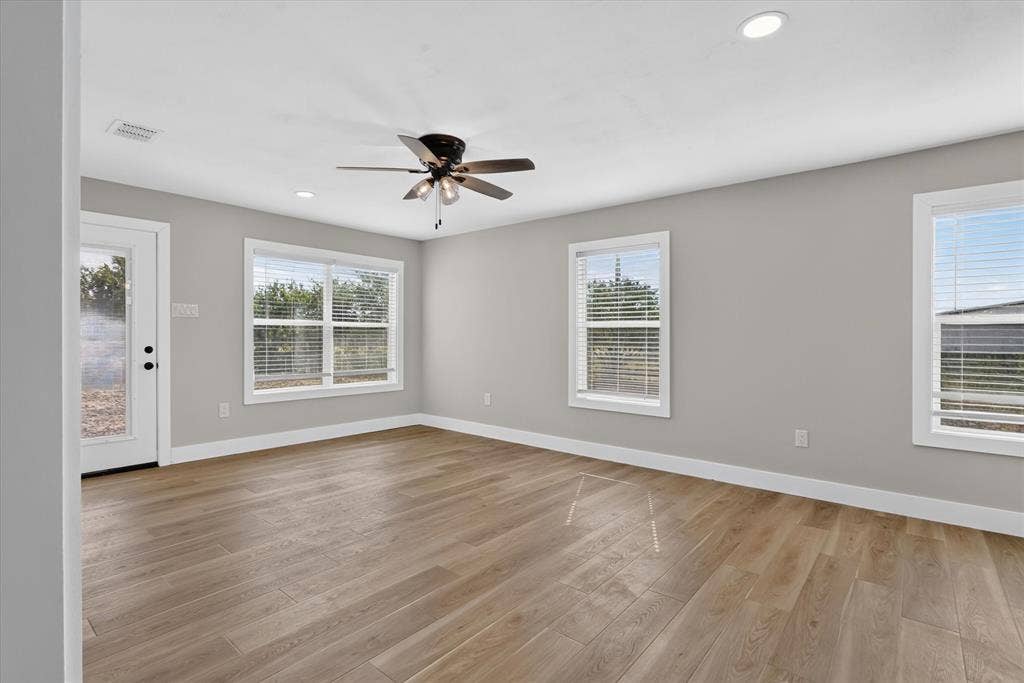 Wood-finish flooring, recessed lighting, ceiling fan, multiple windows, and a white glass-paneled door