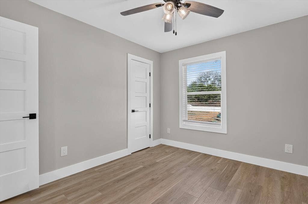 Wood-finish flooring, modern ceiling fan with integrated lighting, window with blinds, contemporary paneled doors, and white trim