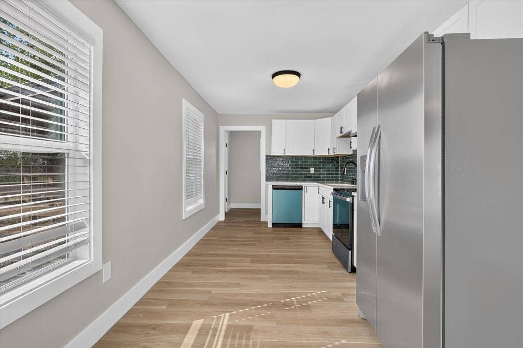 Stainless steel refrigerator and range, integrated dishwasher, subway tile backsplash, white cabinetry, and wood-finish flooring