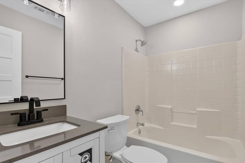 Bathroom featuring a vanity with an integrated sink and countertop, matte black faucet, framed mirror, and a shower-tub combination with tiled walls
