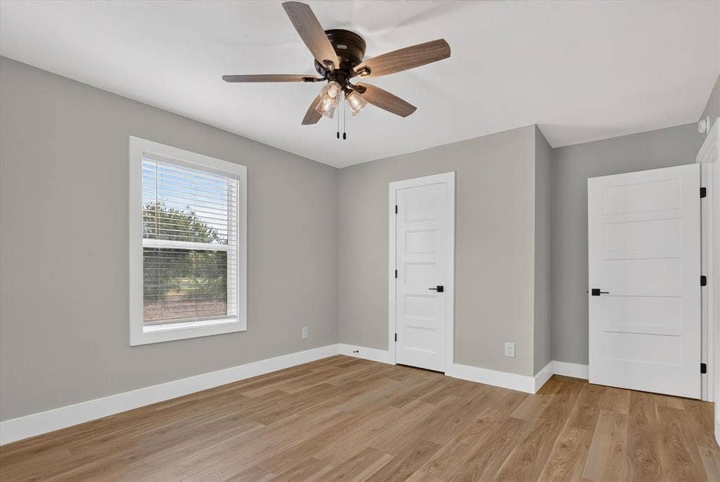 Wood-finish flooring, white trim, a modern ceiling fan with lighting, a window with blinds, and paneled interior doors