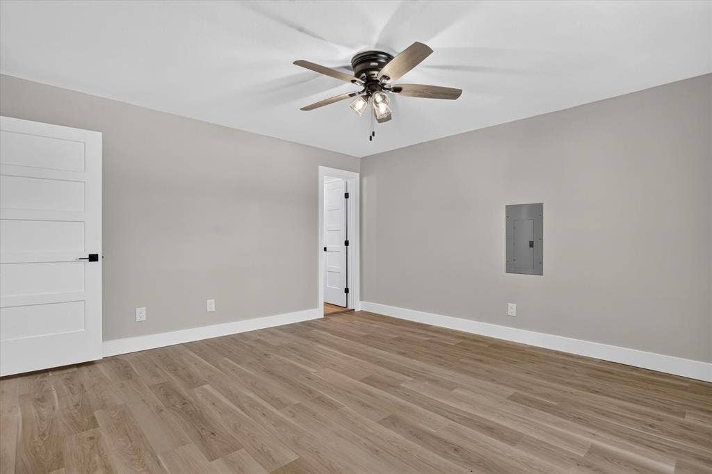 Wood-finish flooring with white baseboards, light gray walls, and a ceiling fan with integrated lighting