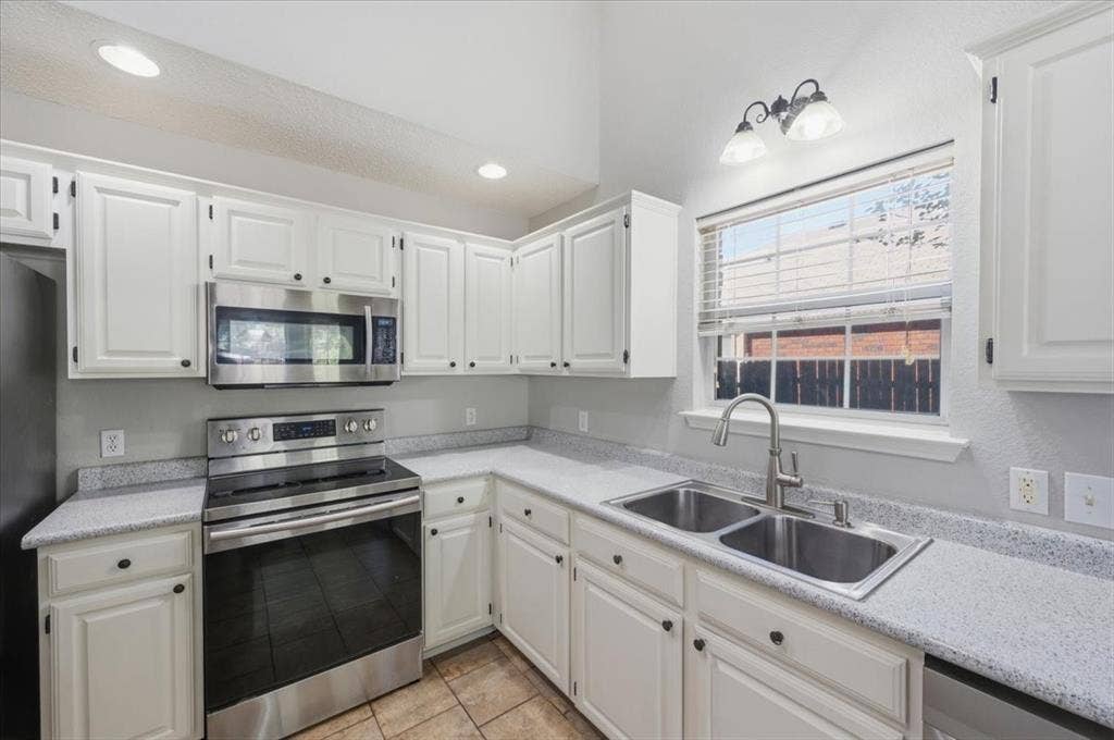 5016 Mill Creek Trail, Fort Worth, TX 76179 Kitchen featuring white cabinetry, light-toned countertops, a stainless steel oven with an overhead microwave, and a double basin sink with a brushed nickel faucet
