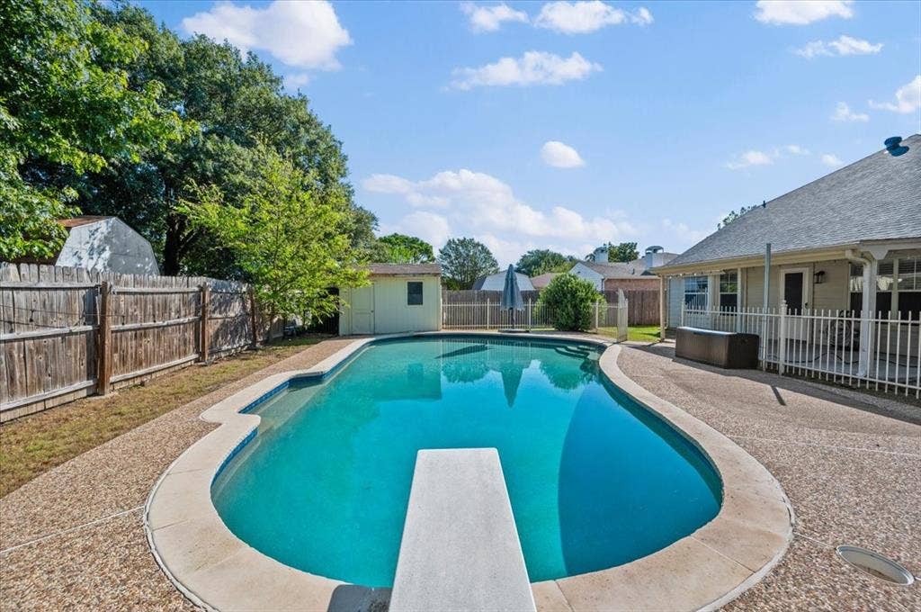 5016 Mill Creek Trail, Fort Worth, TX 76179 Freeform swimming pool with diving board, surrounded by exposed aggregate concrete decking, a white metal fence, and a wood privacy fence
