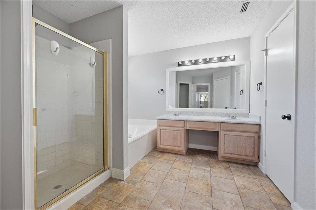 5016 Mill Creek Trail, Fort Worth, TX 76179 Spa-inspired primary bathroom featuring a spacious walk-in shower with glass enclosure and brushed brass fixtures, dual-sink vanity with wood-finish cabinetry and quartz countertop, illuminated mirror with integrated lighting, and neutral tile flooring throughout