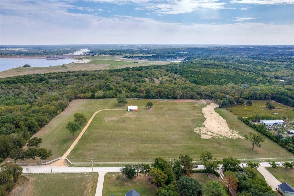 Expansive acreage featuring open pastureland with mature tree lines, a cleared building site with gravel foundation, and direct road frontage