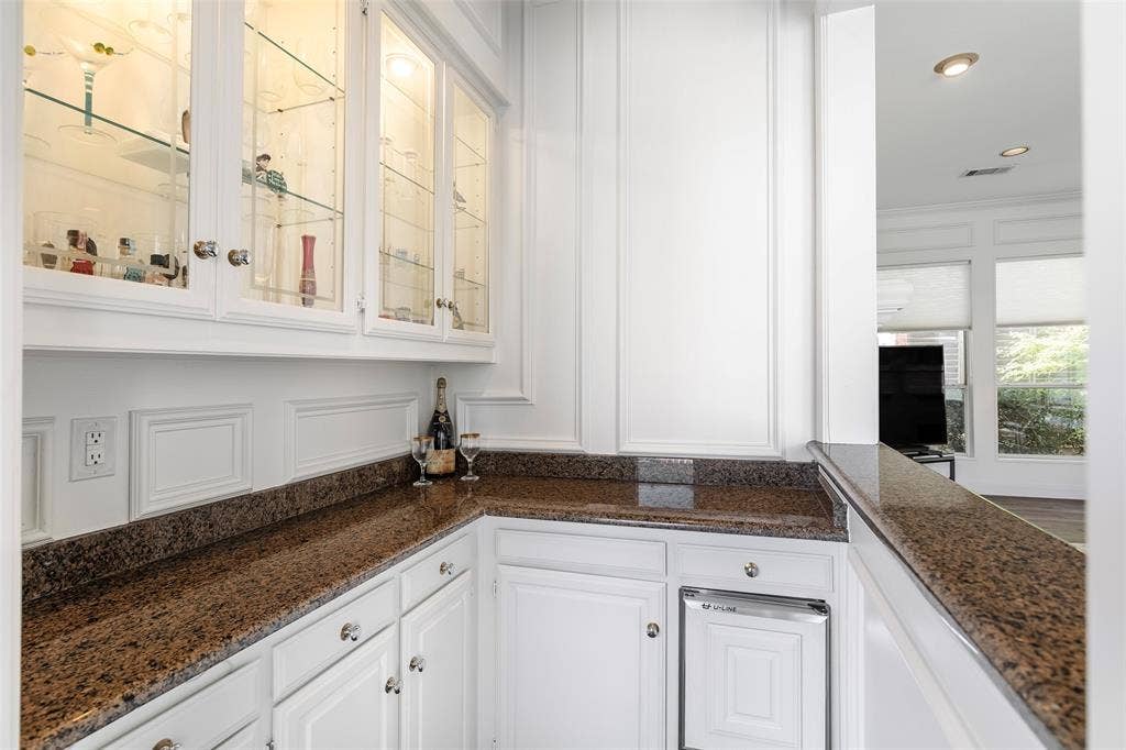 Mix cocktails or serve refreshments effortlessly from your dedicated bar alcove, featuring rich granite countertops, a built-in beverage fridge, and illuminated glass-front display cabinetry.