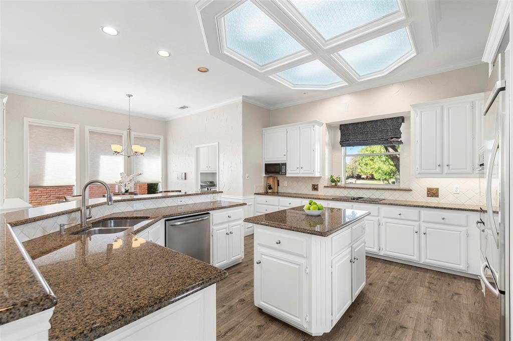 White cabinetry, granite countertops and a center island provide generous storage and preparation space beneath a distinctive ceiling light feature.
