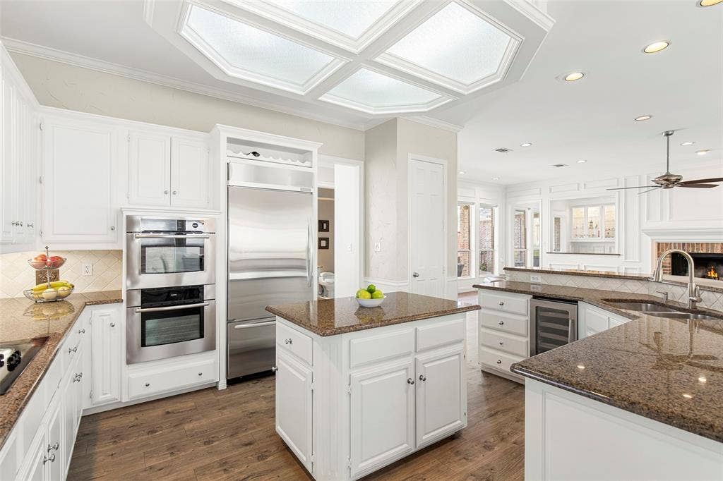 The custom chef's kitchen features built-in double ovens, a premium stainless steel refrigerator with integrated wine storage, granite countertops, and an island that seamlessly transitions into the family room.