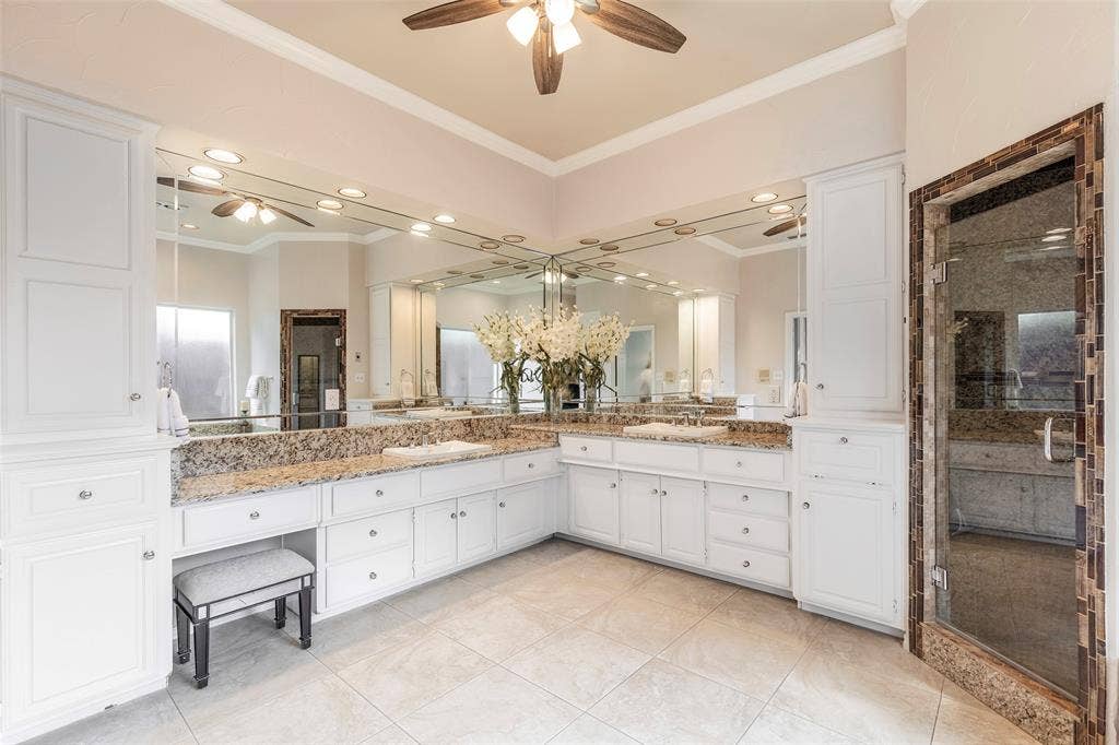 The sprawling primary bathroom boasts expansive L-shaped granite countertops, dual vanities, white cabinetry with built-in storage, and an integrated makeup vanity station