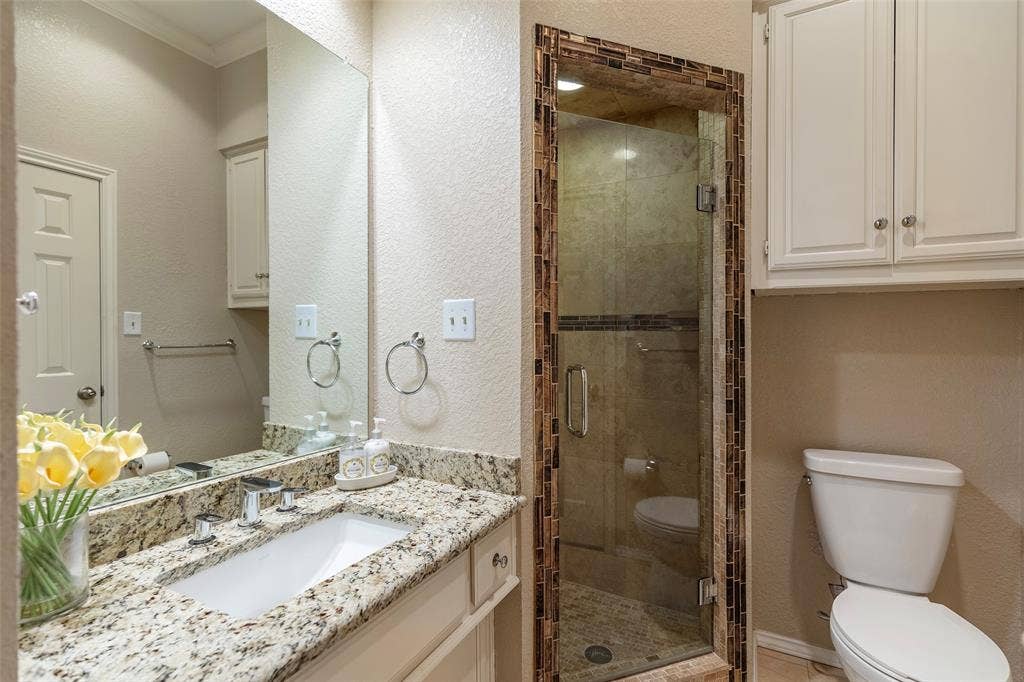 The downstairs full bath features a granite vanity, built-in storage and a glass-enclosed shower, with direct access to the bedroom.