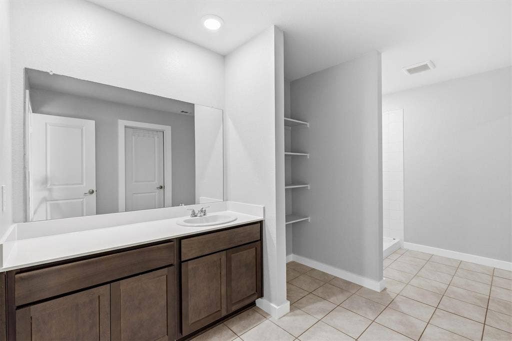 2333 Bellewood Court, Crandall, TX 75114 Spa-inspired primary bathroom featuring a dual-sink vanity with wood-finish cabinetry, white quartz countertop, and an oversized framed mirror