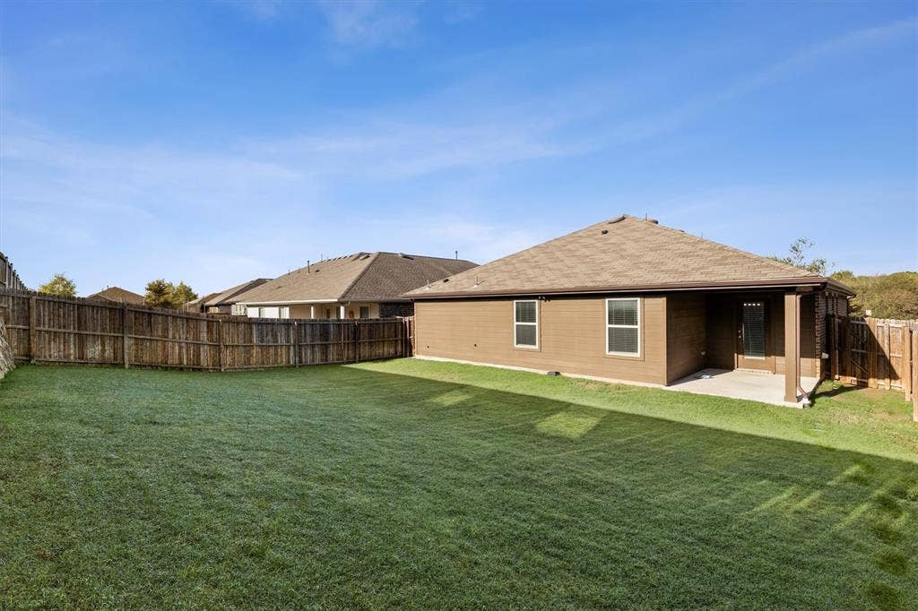2333 Bellewood Court, Crandall, TX 75114 Expansive fenced backyard with a manicured lawn, covered patio, and brown siding