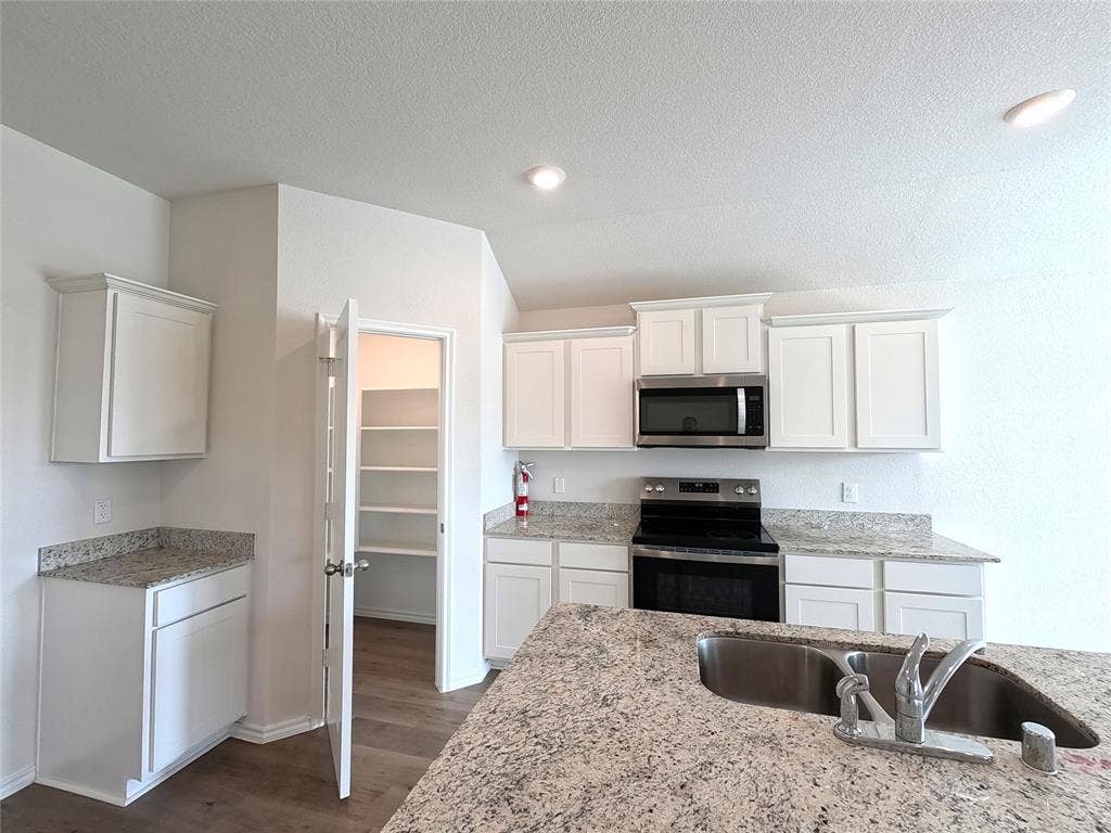 1148 Samantha Drive, Dallas, TX 75253 Kitchen featuring white cabinetry, granite-finish countertops, stainless steel microwave, black electric range, and a built-in pantry with shelving
