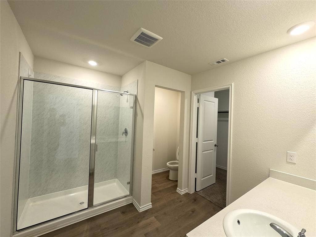 1148 Samantha Drive, Dallas, TX 75253 Glass-enclosed shower with a white base, white walls, wood-finish flooring, a white countertop with an integrated sink, and recessed lighting