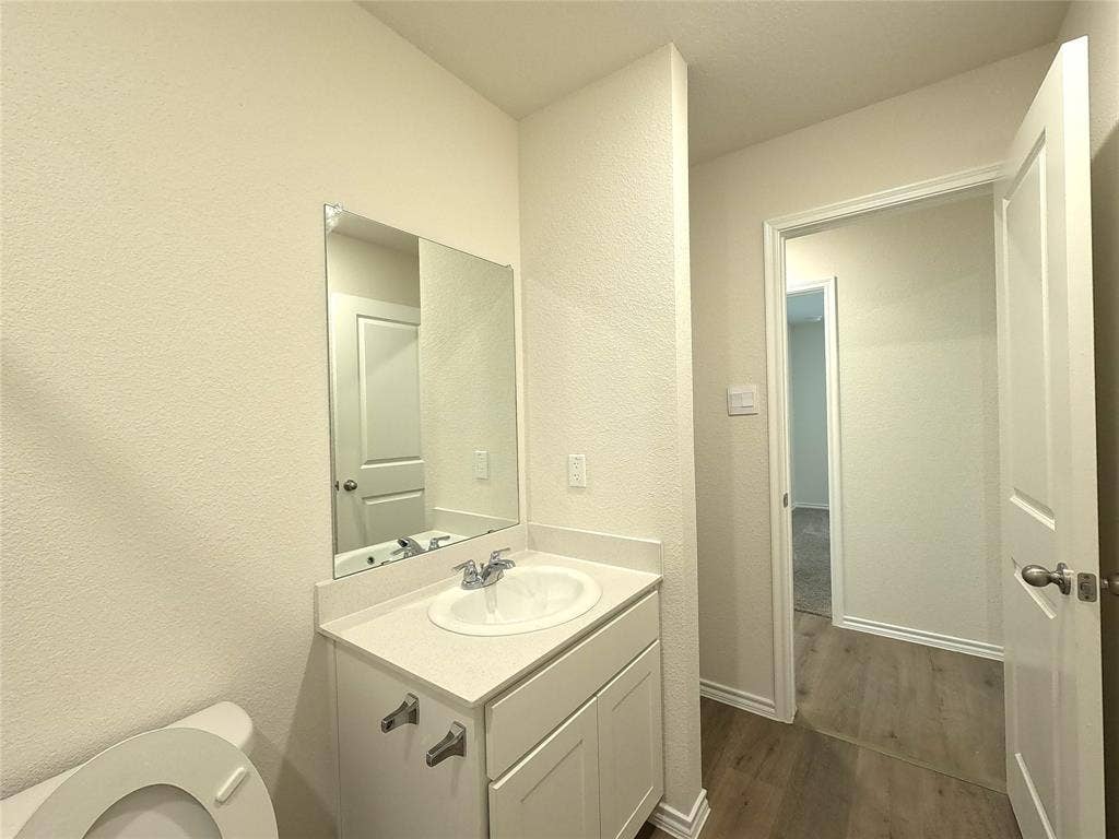 1148 Samantha Drive, Dallas, TX 75253 Vanity with an integrated sink and chrome faucet, large frameless mirror, and a wood-finish flooring
