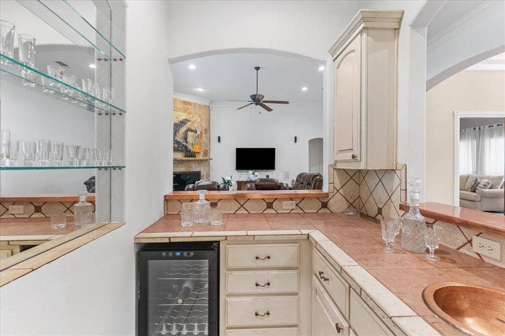 117 Redtail Court, Weatherford, TX 76088 Built-in wet bar featuring tile countertops, copper sink, glass shelving, cabinetry, and a dedicated beverage cooler