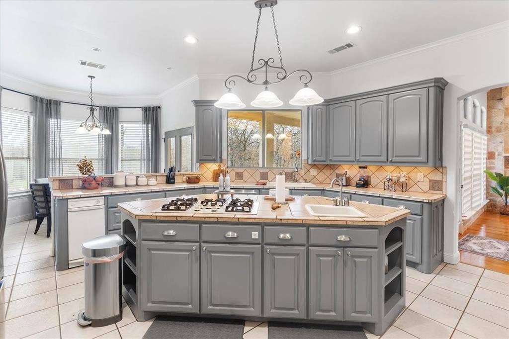 117 Redtail Court, Weatherford, TX 76088 Kitchen featuring gray cabinetry, a central island with a built-in gas cooktop and sink, tile countertops with matching backsplash, and decorative pendant lighting