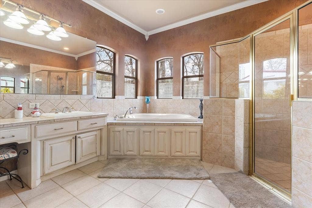 117 Redtail Court, Weatherford, TX 76088 Bathroom featuring a dual-sink vanity with light cabinetry, tiled soaking tub surround, arched windows, and a glass-enclosed shower with tiled walls