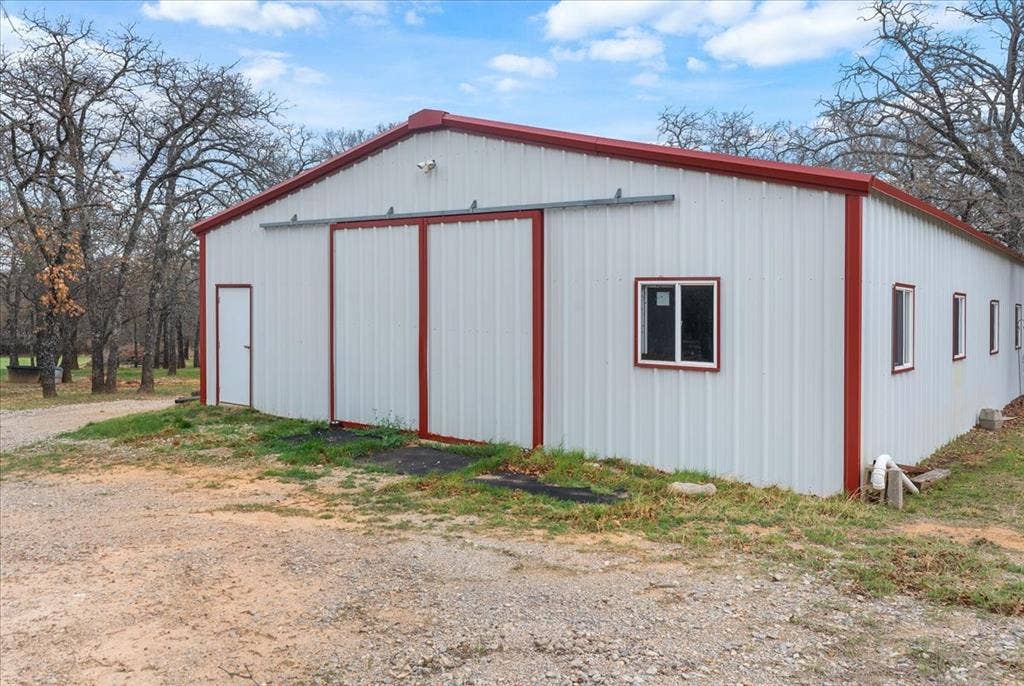 117 Redtail Court, Weatherford, TX 76088 Modern metal-frame agricultural or commercial building featuring a distinctive peaked roof with red trim accents, white corrugated metal siding, and multiple window openings for natural light