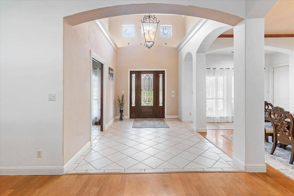 117 Redtail Court, Weatherford, TX 76088 Grand entryway featuring high ceilings, a decorative wrought-iron chandelier, porcelain tile flooring set on a diagonal, and a wooden front door with glass insets framed by architectural arches