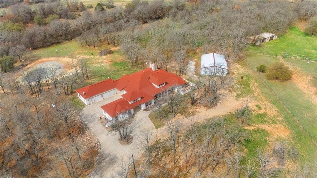 117 Redtail Court, Weatherford, TX 76088 Aerial view of property featuring a multi-gabled roofline, concrete driveway, attached garage, detached metal building, and private pond