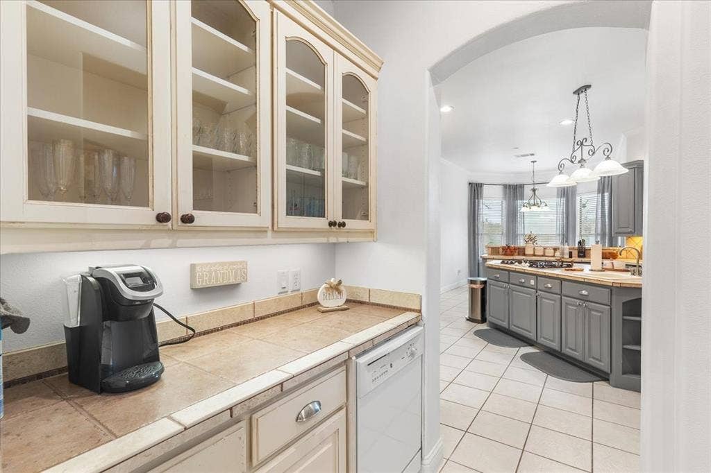 117 Redtail Court, Weatherford, TX 76088 Custom off-white cabinetry with glass-front uppers, ceramic tile countertops, built-in dishwasher, and arched architectural detailing