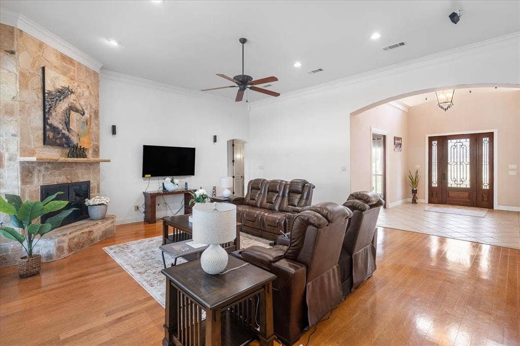 117 Redtail Court, Weatherford, TX 76088 Living room featuring wood-finish flooring, a floor-to-ceiling stone-surround fireplace with a wooden mantel, recessed lighting, and an arched entryway leading to a foyer with a wood-framed glass-paneled door