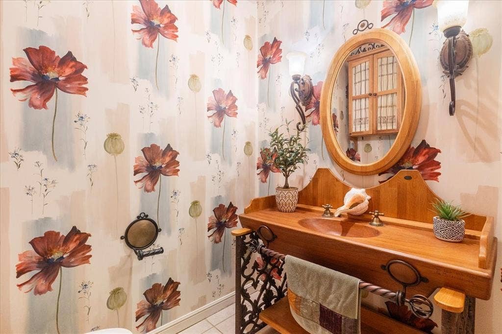 117 Redtail Court, Weatherford, TX 76088 Charming guest powder bathroom featuring floral-patterned wallcovering, wood-finish vanity with integrated shelving, oval wood-framed mirror, and decorative wall-mounted fixtures