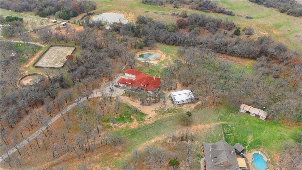 117 Redtail Court, Weatherford, TX 76088 Aerial perspective of expansive acreage featuring a primary residence with a metal roof, dedicated equestrian arena, round pen, multiple outbuildings, and natural ponds