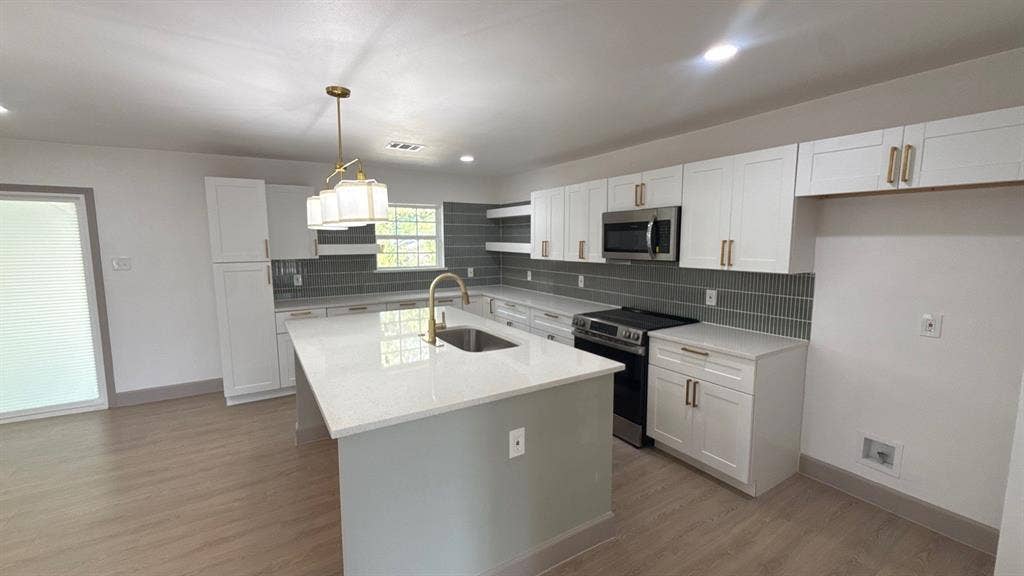 7437 Eccles Drive, Dallas, TX 75227 Kitchen featuring white shaker cabinetry, quartz countertops, a central island with a stainless steel undermount sink, a tiled backsplash, and wood-finish flooring