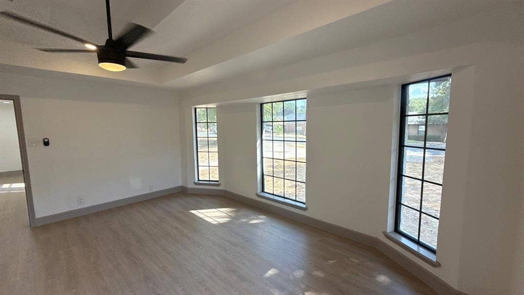 7437 Eccles Drive, Dallas, TX 75227 Tray ceiling with a matte black modern ceiling fan, wood-finish flooring, and expansive windows featuring dark frames