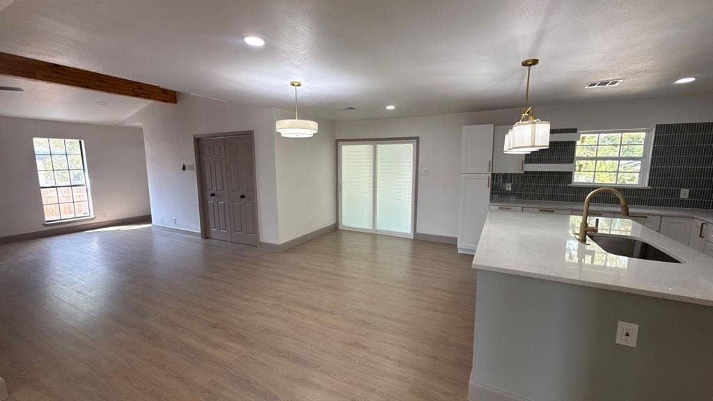 7437 Eccles Drive, Dallas, TX 75227 Open-concept kitchen featuring an island with a light-toned countertop, custom cabinetry, tiled backsplash, wood-finish flooring, and exposed ceiling beams