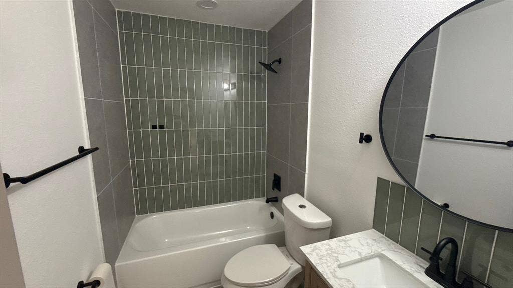 7437 Eccles Drive, Dallas, TX 75227 Bathroom featuring a tub with vertical green tile surround, vanity with stone-patterned countertop, matte black faucet, and a round wall-mounted mirror
