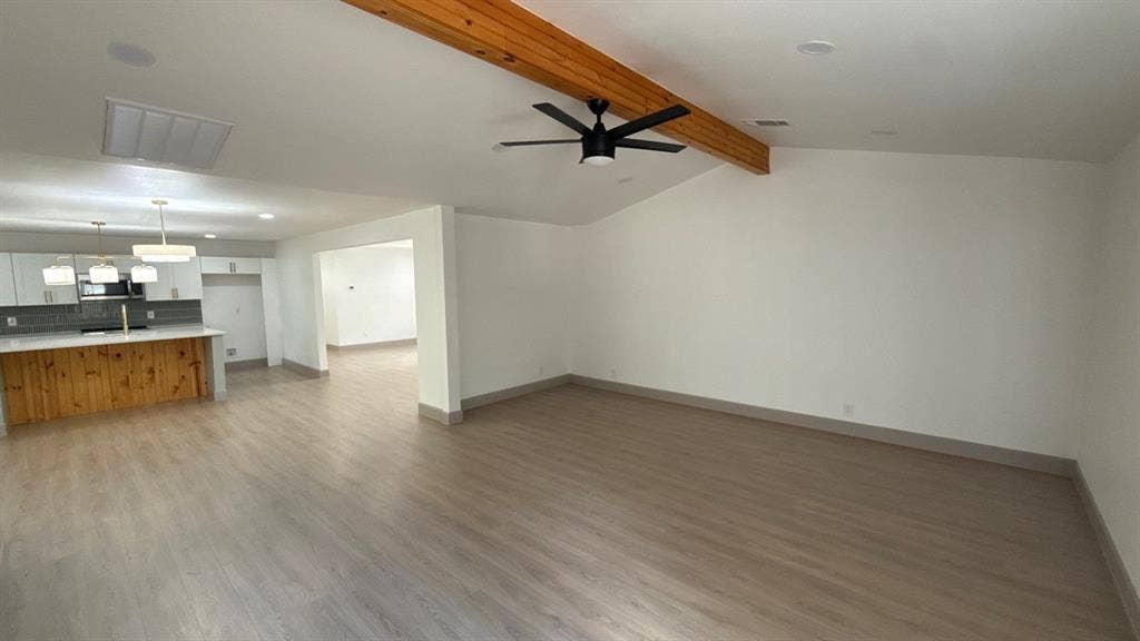 7437 Eccles Drive, Dallas, TX 75227 Open-concept interior featuring wood-finish flooring, a vaulted ceiling with an exposed wood beam, a matte black ceiling fan, recessed lighting, and a kitchen island with built-in wood cabinetry