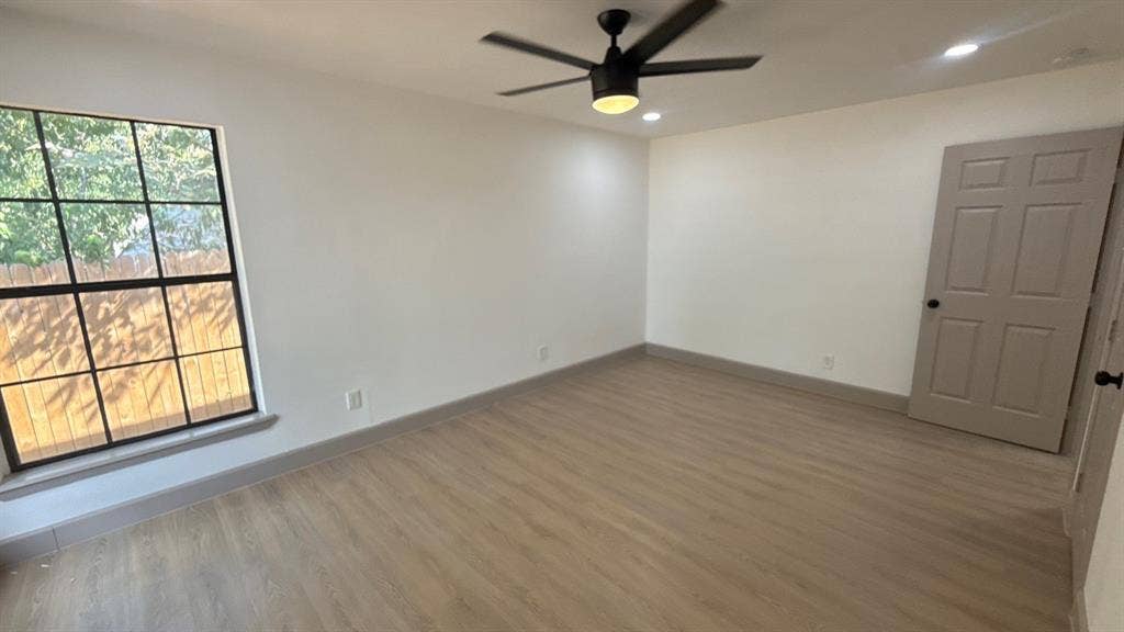 7437 Eccles Drive, Dallas, TX 75227 Interior room featuring wood-finish flooring, a multi-pane window with black framing, a matte black ceiling fan with an integrated light fixture, and a neutral-toned paneled door