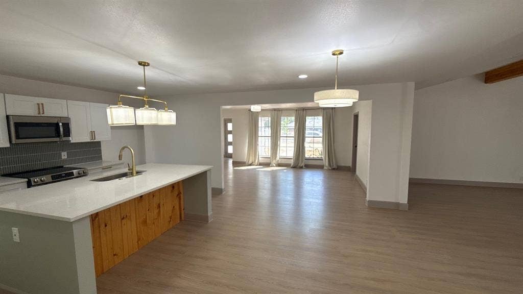 7437 Eccles Drive, Dallas, TX 75227 Kitchen featuring a central island with wood paneling and a quartz countertop, white cabinetry, integrated stainless steel appliances, and gold-finish pendant lighting, complemented by neutral wood-finish flooring throughout the space
