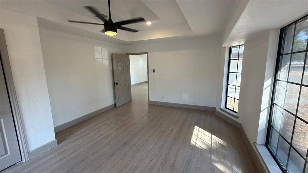 7437 Eccles Drive, Dallas, TX 75227 Interior space featuring wood-finish flooring, a tray ceiling with a matte black ceiling fan, and large windows with black mullions