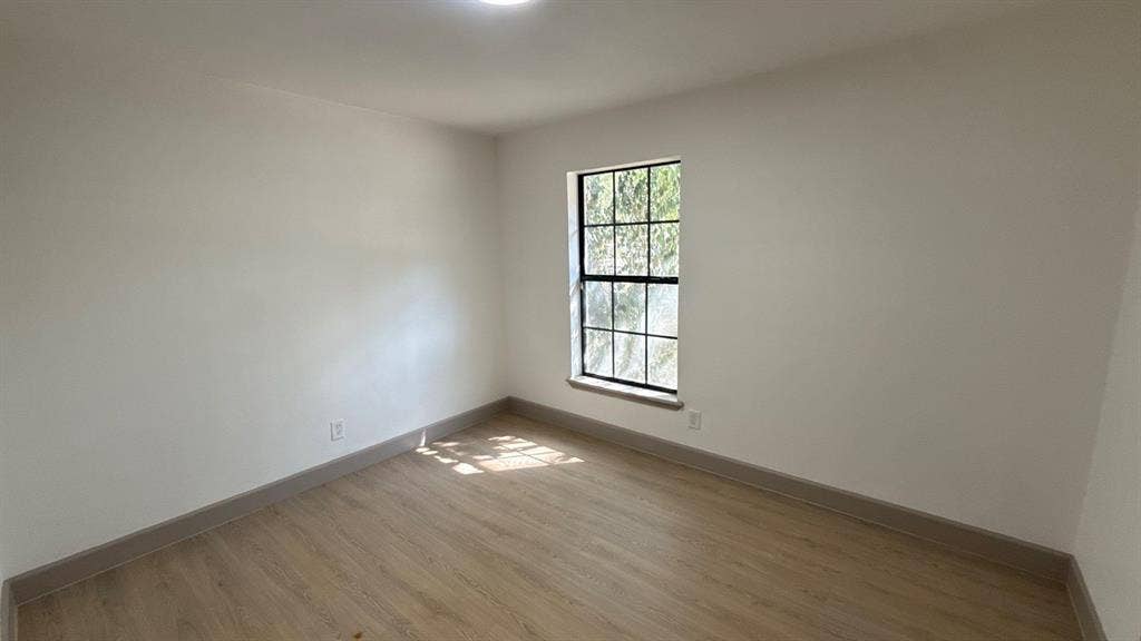 7437 Eccles Drive, Dallas, TX 75227 Neutral-toned walls, wood-finish flooring, and a single-hung window with a dark-finish frame