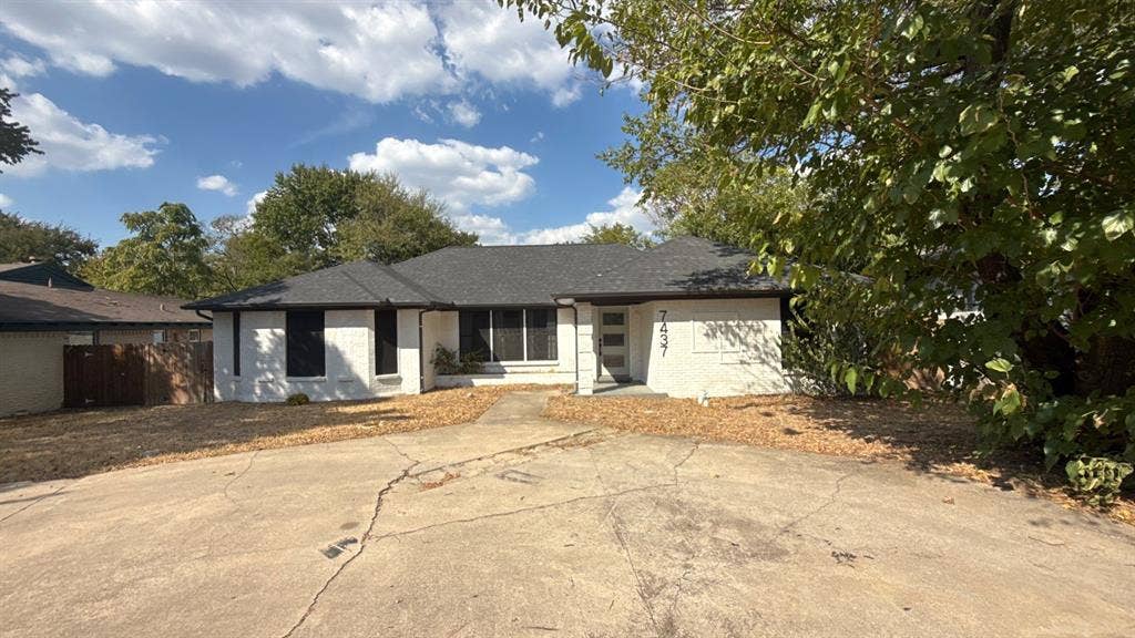 7437 Eccles Drive, Dallas, TX 75227 Single-story exterior featuring a white painted brick facade, dark roofing shingles, multi-pane windows, and a paved circular driveway