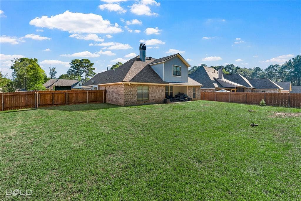 Expansive backyard featuring a manicured lawn, full-perimeter wood fencing, brick and lap siding exterior, and a chimney stack